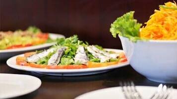 Een eettafel met borden eten, waaronder een salade met sla en geraspte wortelen, en een schaal met geraspte wortelen.