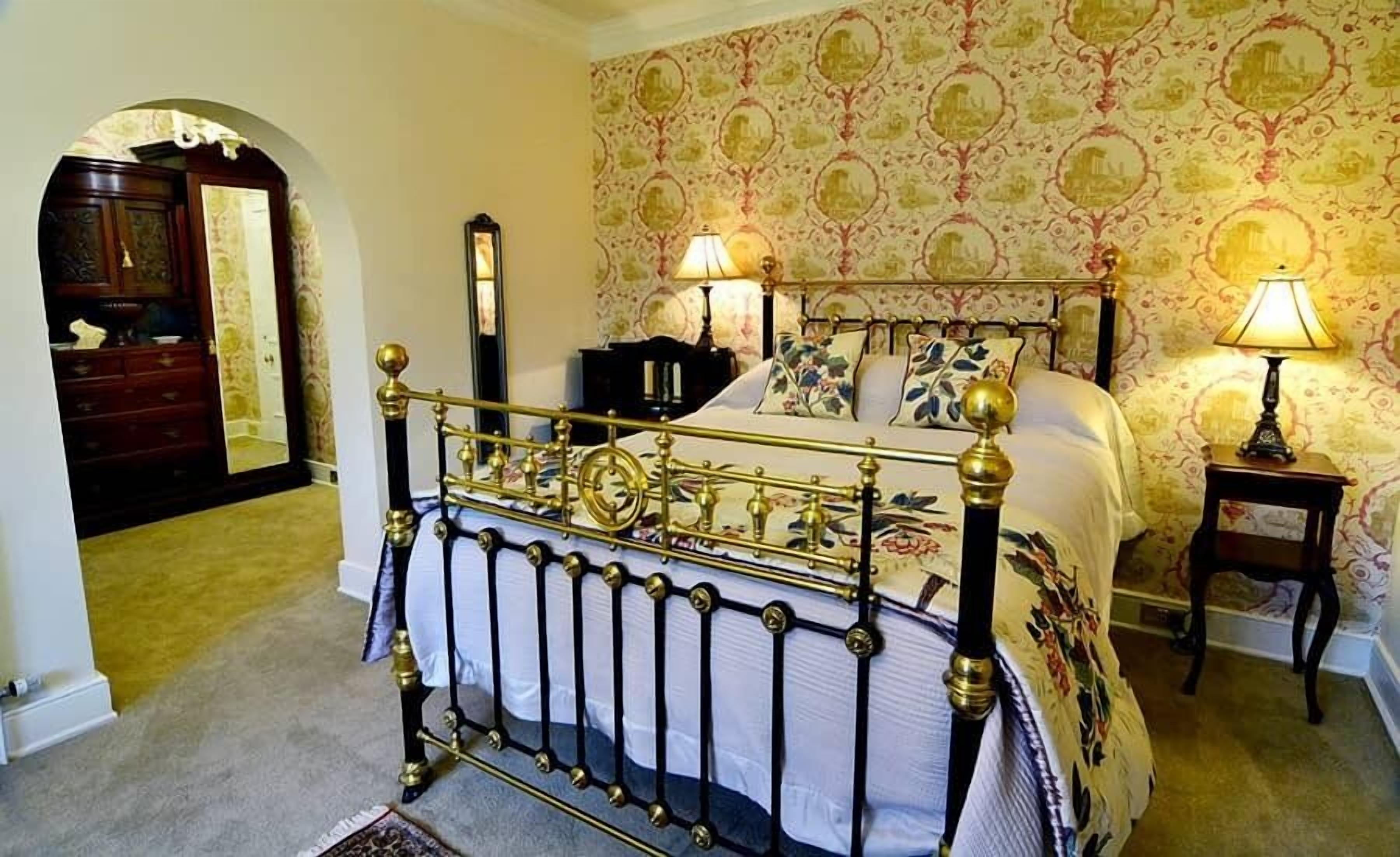 A bedroom with a classic four-poster bed, a wooden wardrobe, and a mirror.