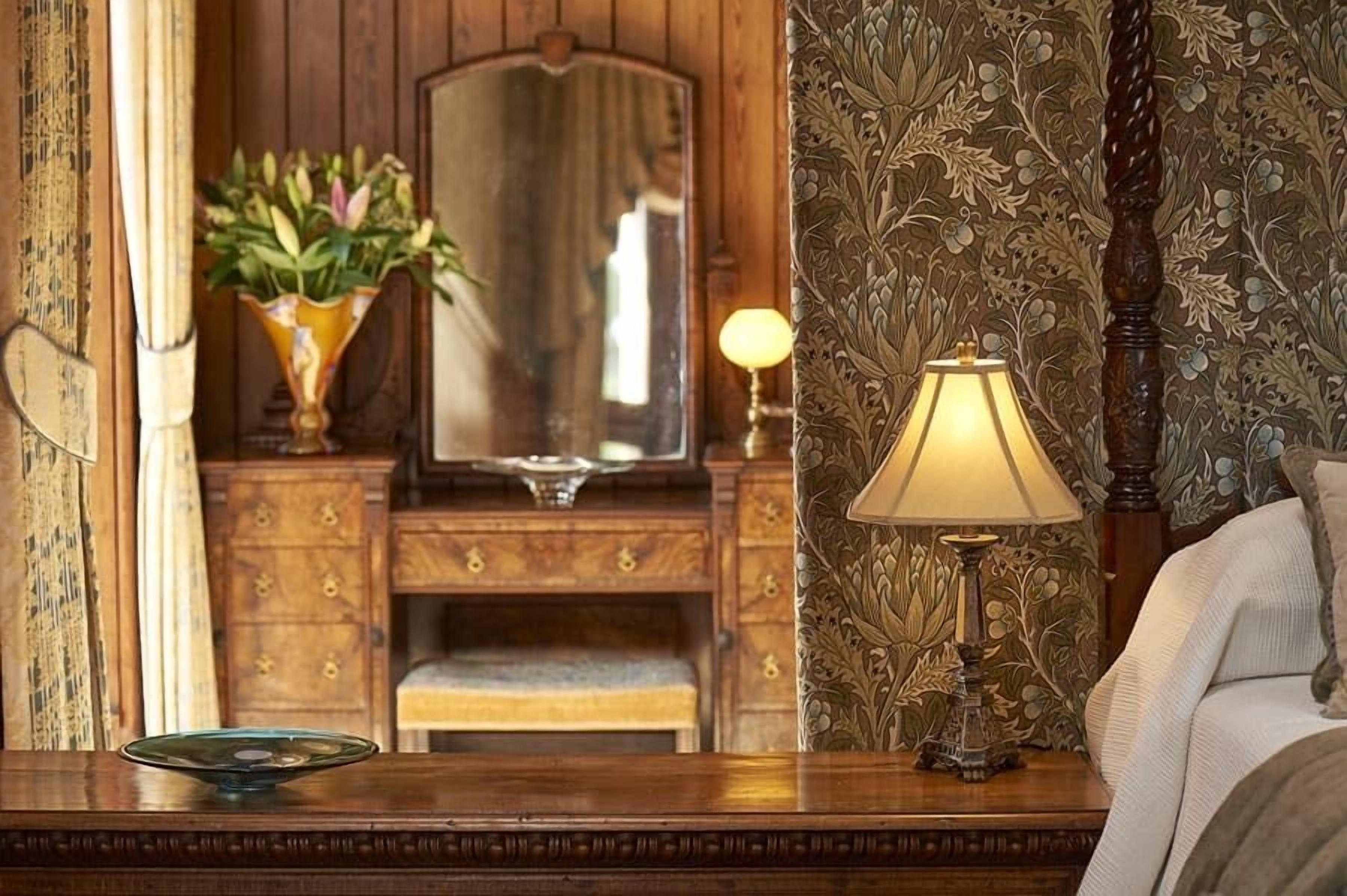 A wooden dresser with a mirror, a lamp, and a vase with flowers.