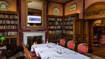Una biblioteca con estanterías, una chimenea, una mesa dispuesta para comer y un espejo grande.