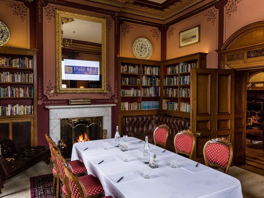 Una biblioteca con estanterías, una chimenea, una mesa dispuesta para comer y un espejo grande.