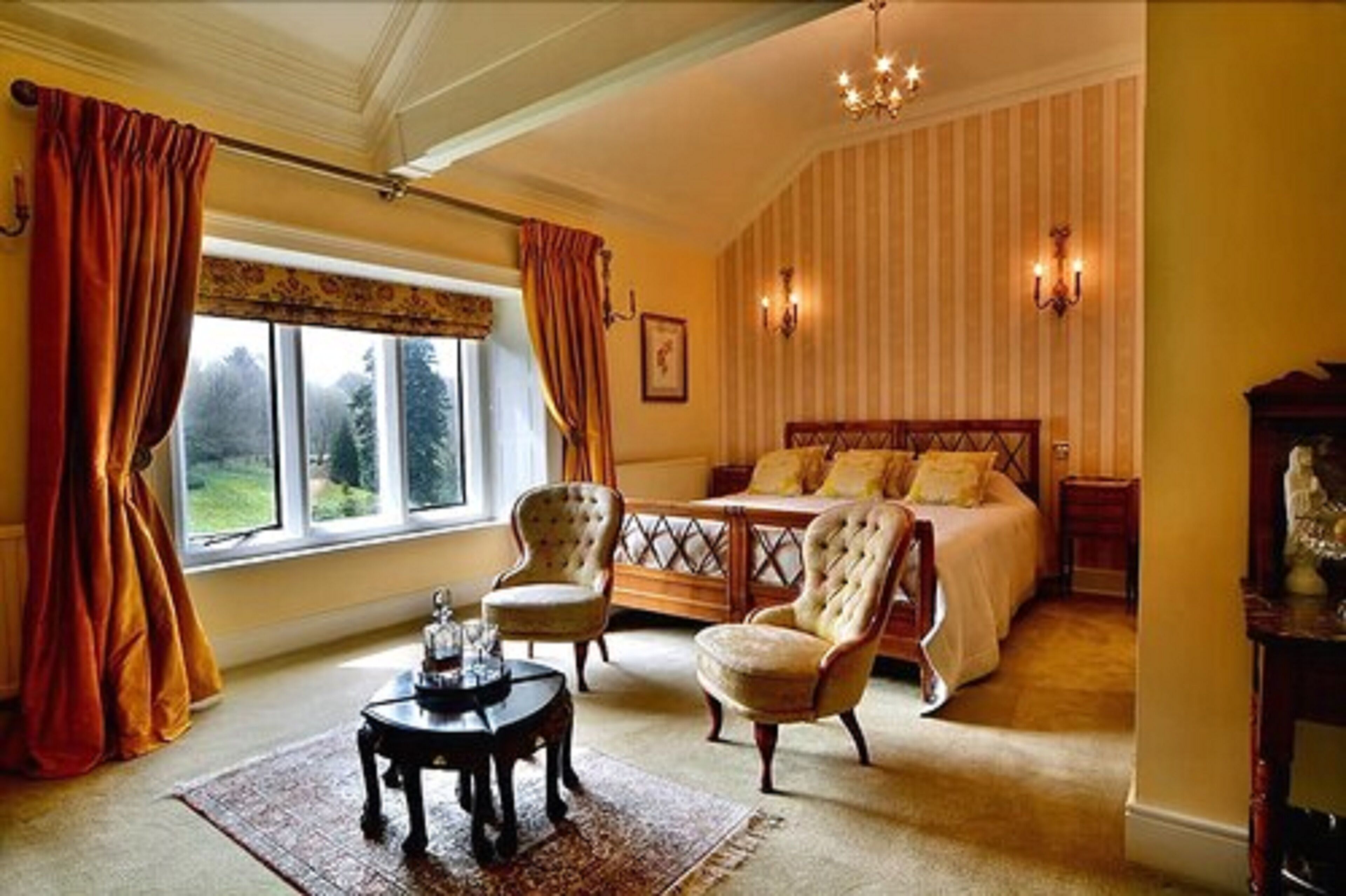 Een slaapkamer met een groot bed, twee fauteuils, een bijzettafeltje en uitzicht op het landschap door een raam.