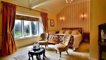 Een slaapkamer met een groot bed, twee fauteuils, een bijzettafeltje en uitzicht op het landschap door een raam.