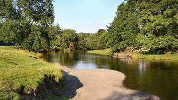A river with a gravel path alongside it, surrounded by dense green trees.