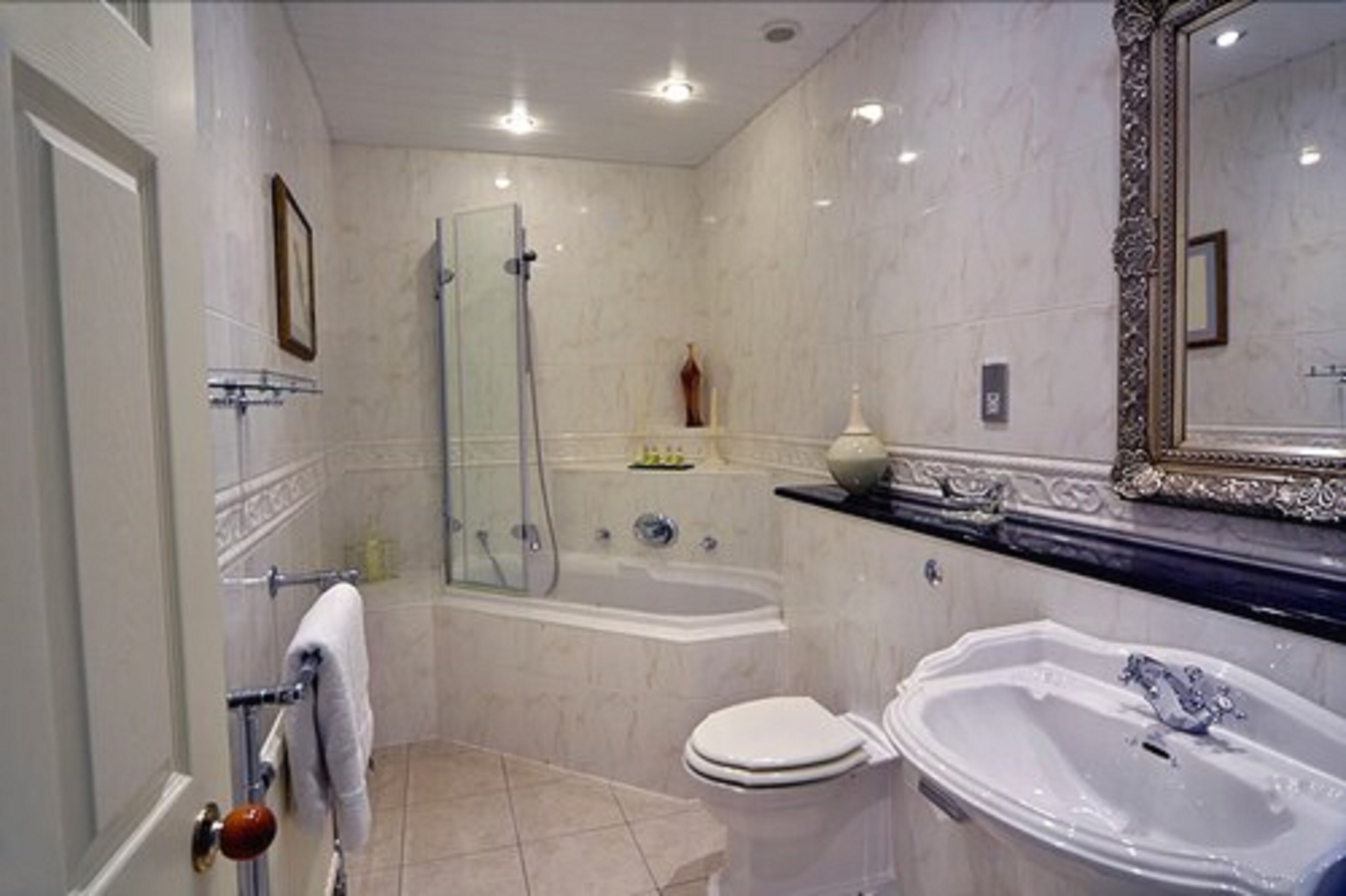 A bathroom with a bathtub, toilet, and sink, featuring marble walls and a large mirror.