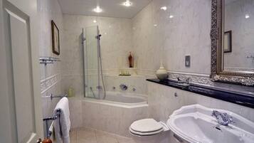 A bathroom with a bathtub, toilet, and sink, featuring marble walls and a large mirror.