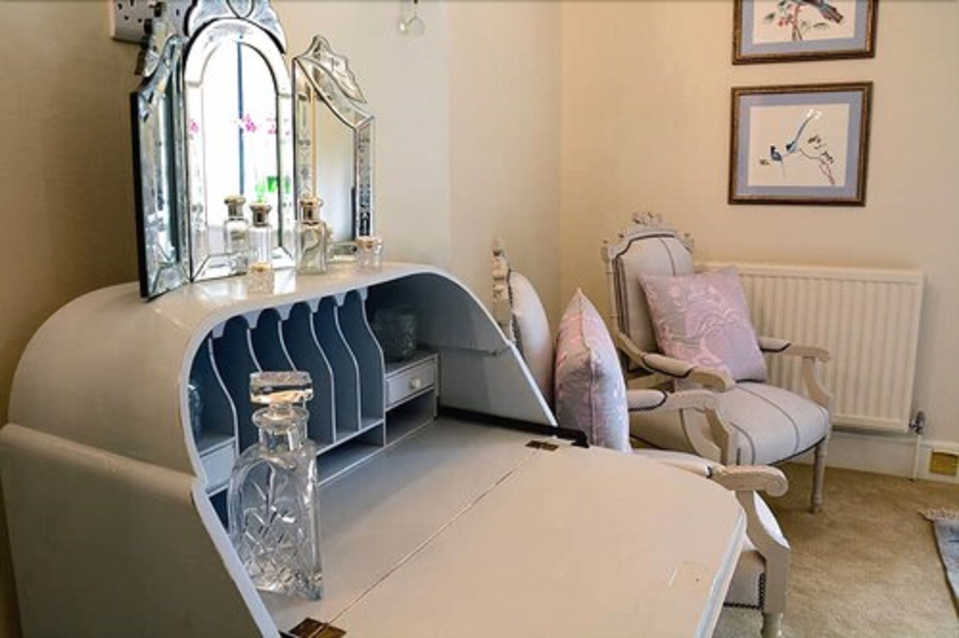 A bedroom with a vanity, a mirror, a chair, and two framed pictures on the wall.