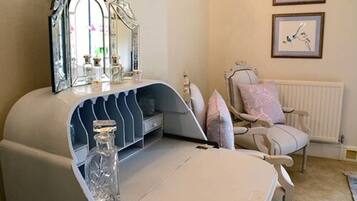 A bedroom with a vanity, a mirror, a chair, and two framed pictures on the wall.