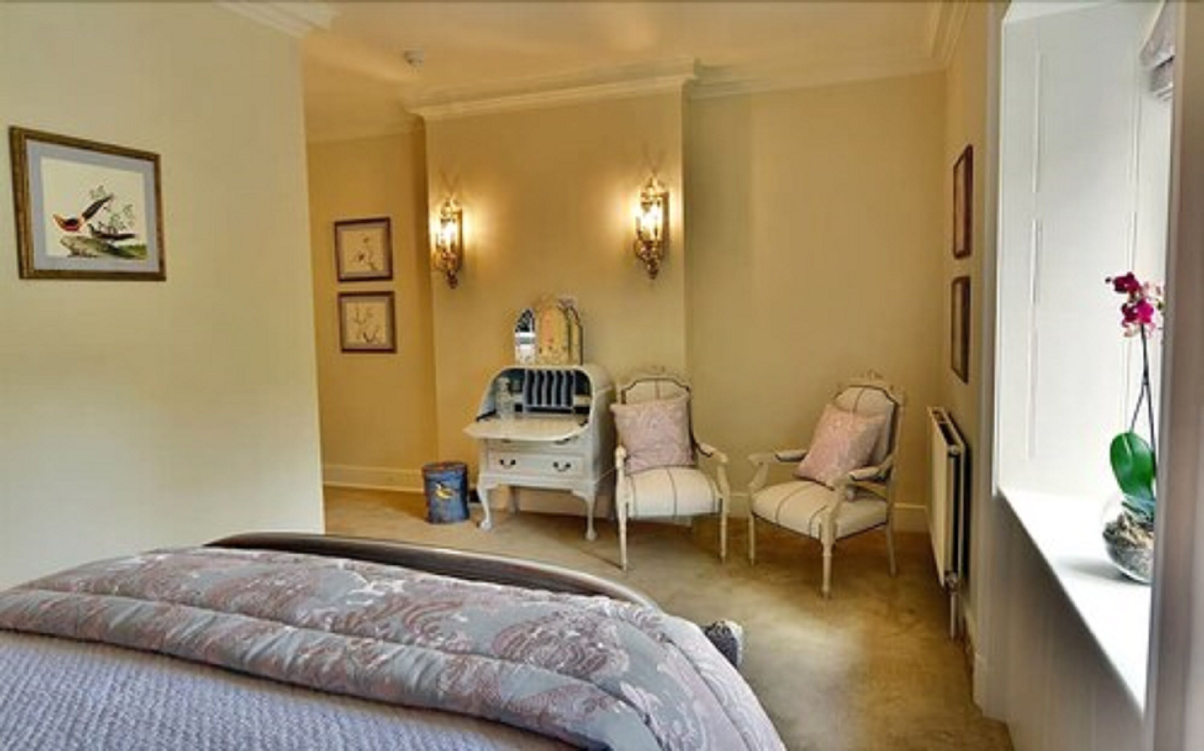 A bedroom with a bed, two chairs, a dresser, and wall-mounted lights.