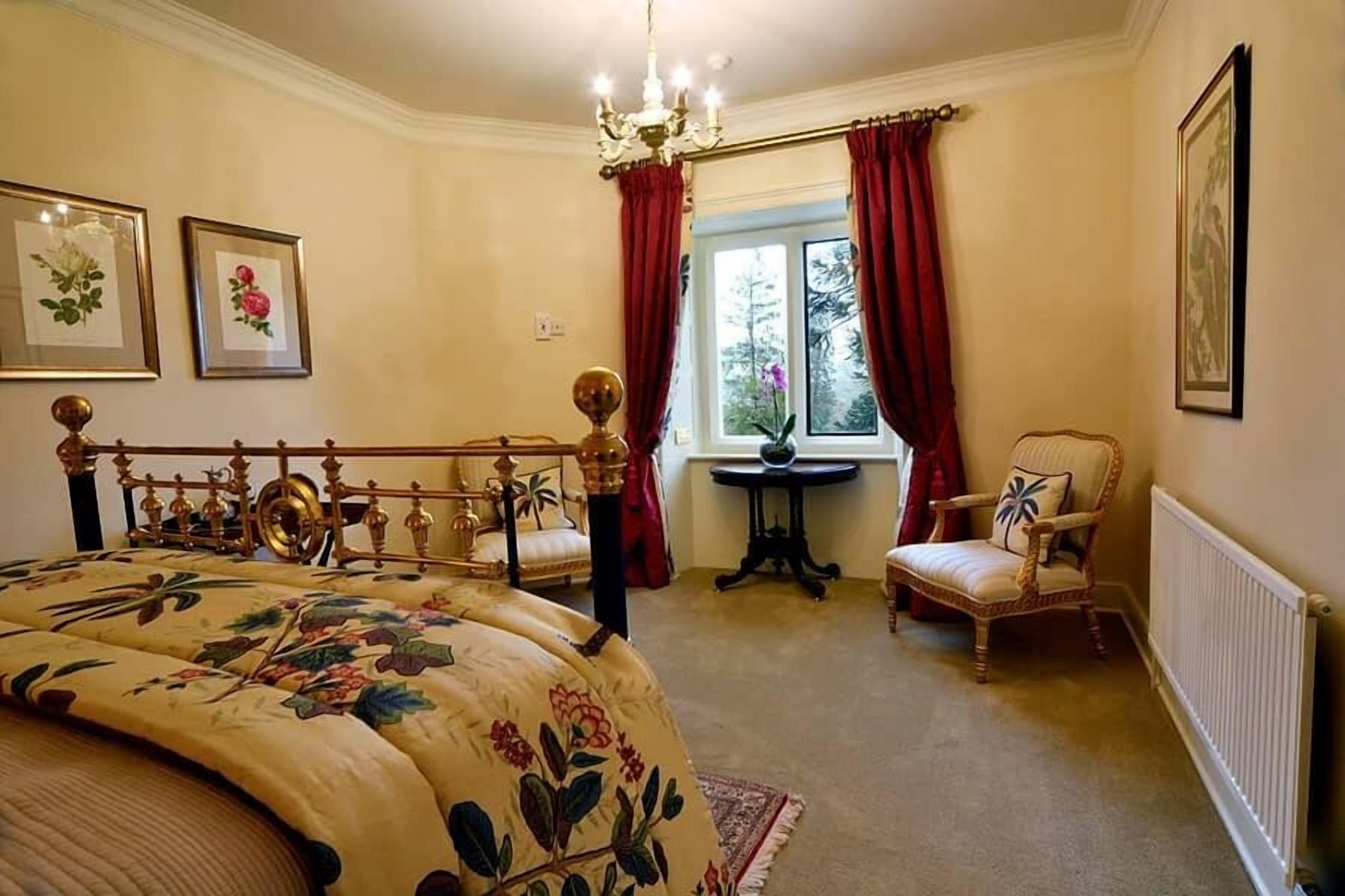 A bedroom with a bed, a chair, a table, and a window with curtains.
