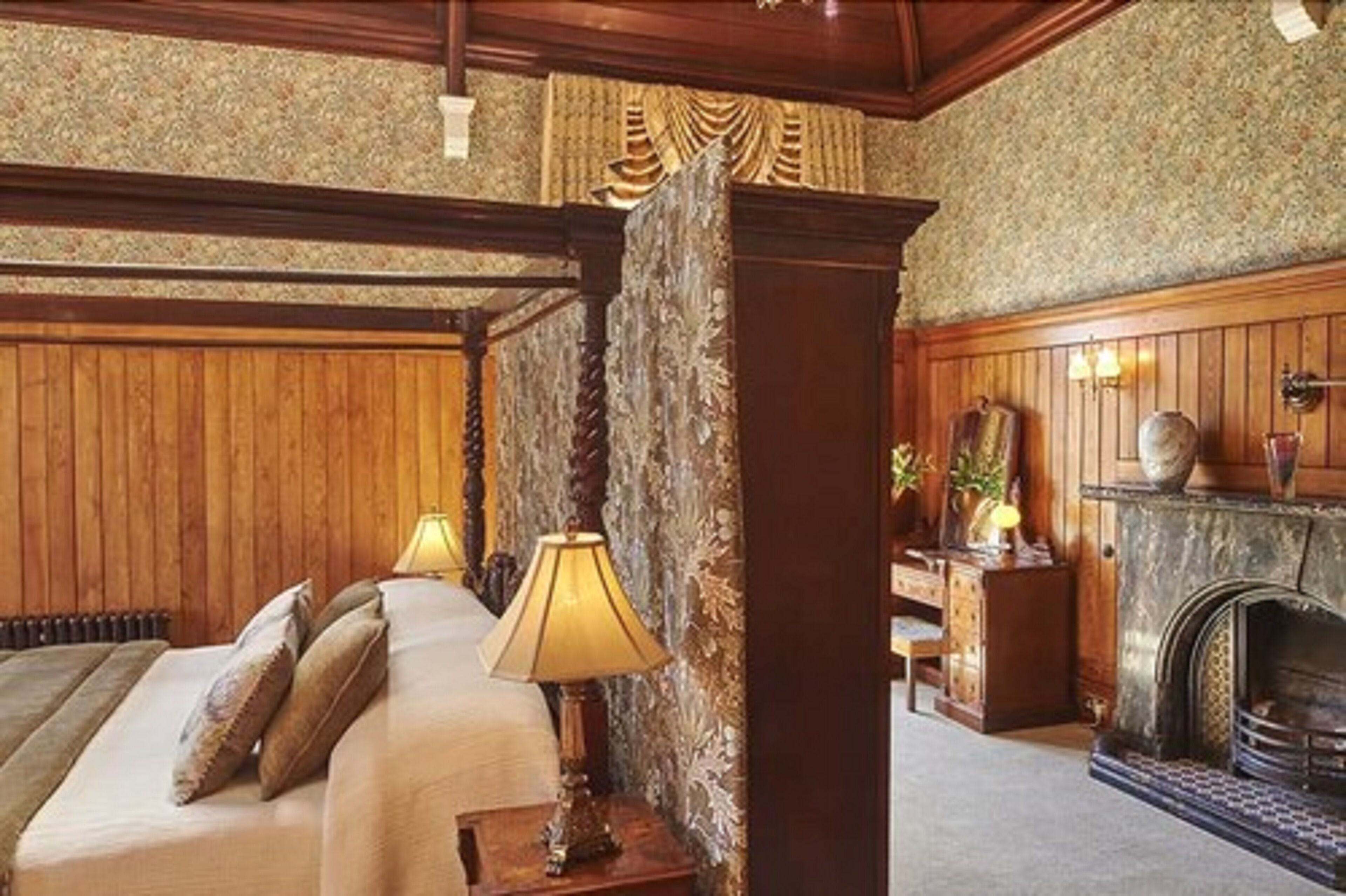 Una habitación tradicional con paneles de madera, una cama con mesita de noche, un escritorio con lámpara y una chimenea.