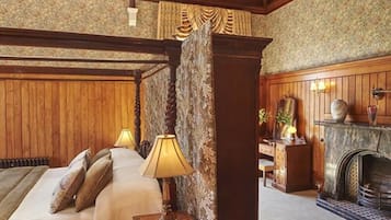 Una habitación tradicional con paneles de madera, una cama con mesita de noche, un escritorio con lámpara y una chimenea.
