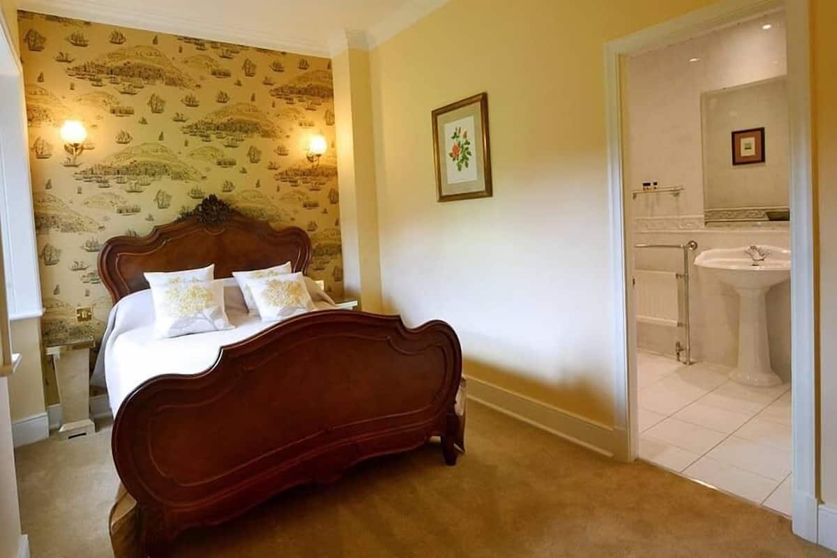 Une chambre à coucher avec un lit en bois, une salle de bain avec un lavabo et un miroir, et un papier peint à motifs.