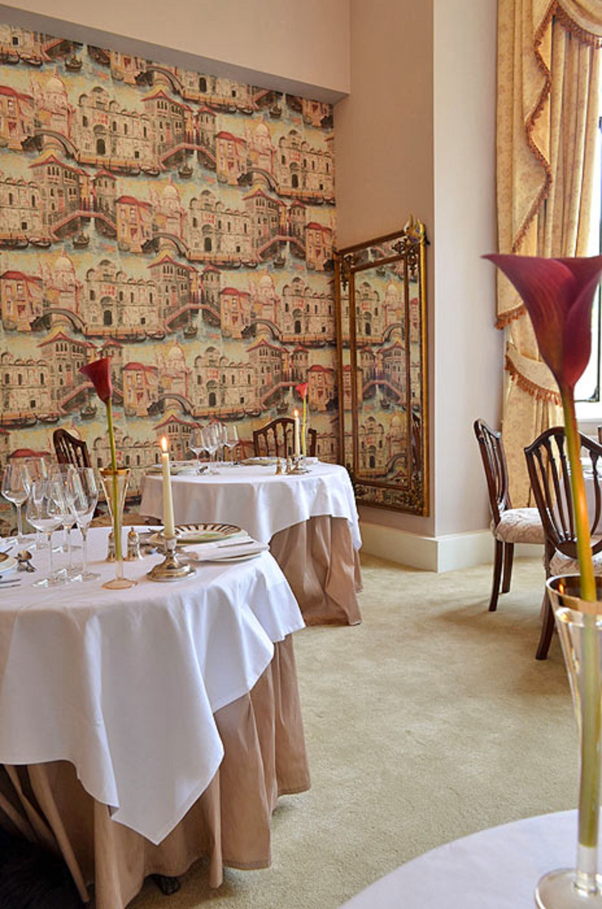 A dining area with tables set for a meal, a patterned wall, and a large mirror.