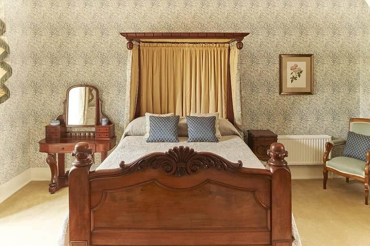 Une chambre à coucher avec un lit à baldaquin, une commode en bois, un miroir et un tableau encadré accroché au mur.