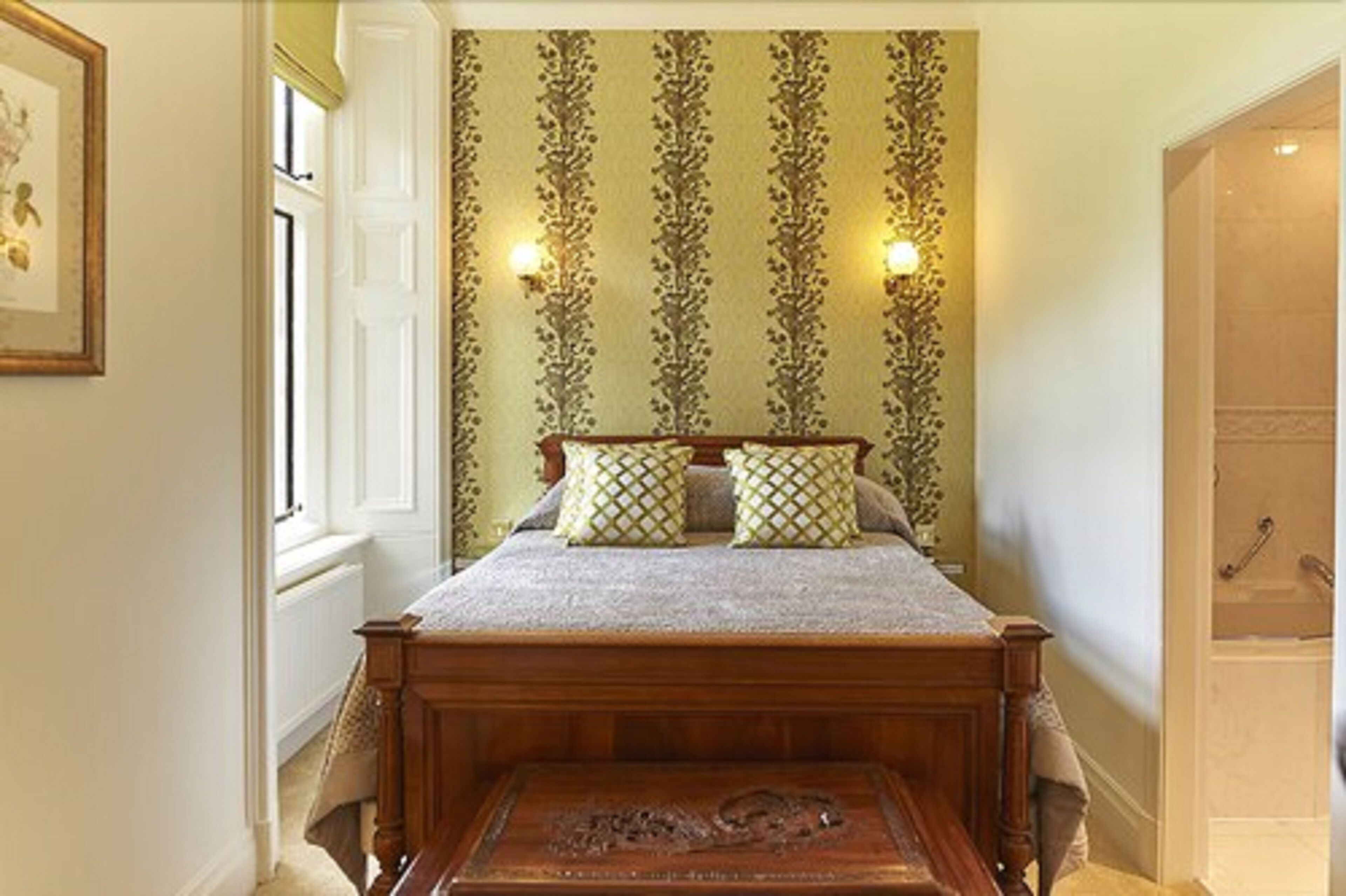 A bedroom with a wooden bed, patterned wallpaper, and two wall-mounted lights.