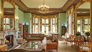 Une vaste pièce dotée d’une cheminée, de meubles richement décorés et de grandes fenêtres.