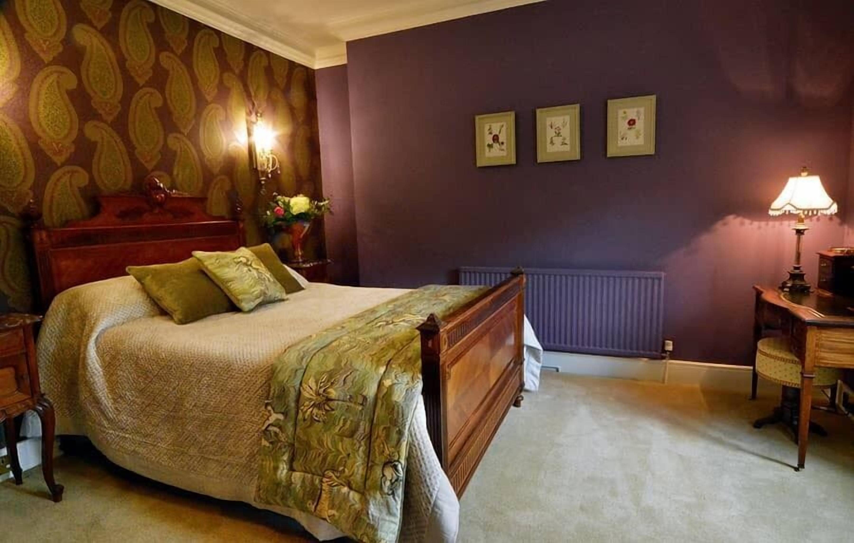A bedroom with a bed, a dresser, a nightstand, a lamp, and a radiator.