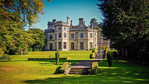 Un grand bâtiment historique à la façade symétrique, doté de nombreuses cheminées et agrémenté d’un jardin bien entretenu, avec un escalier central menant à l’entrée.