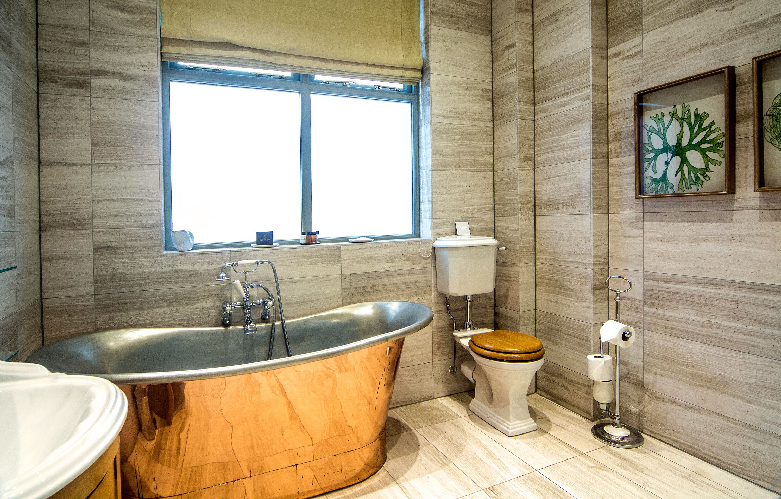 Une salle de bain moderne avec une baignoire sur pieds, des toilettes et une fenêtre laissant entrer la lumière naturelle.
