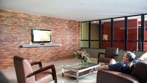 Una sala de estar moderna con un televisor sobre una pared de ladrillo, una mesa de centro de cristal con flores y sofás de cuero.