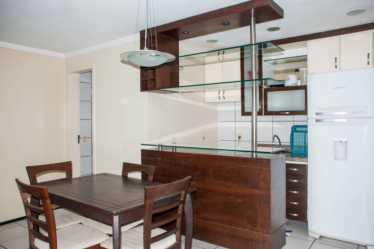 Una cocina moderna con una mesa de comedor de madera, sillas, una isla con cubierta de vidrio y un refrigerador blanco.