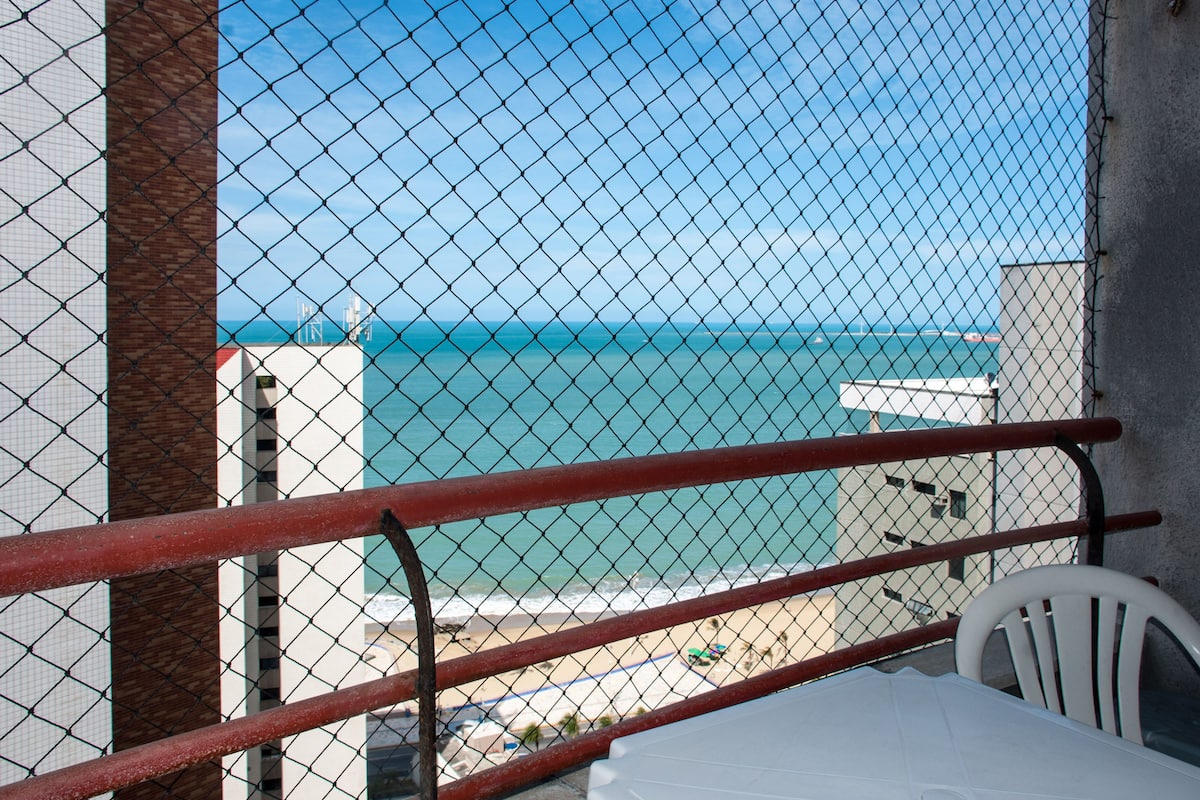 Un balcón con vista al mar, una mesa blanca y una silla blanca.