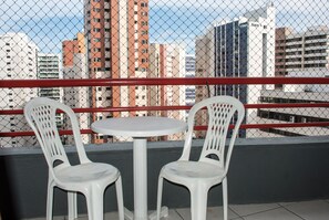 A balcony with two white plastic chairs and a small round table, overlooking a cityscape with tall buildings.