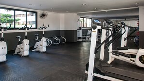 Un gimnasio con bicicletas estáticas, cintas de correr y un ventilador.