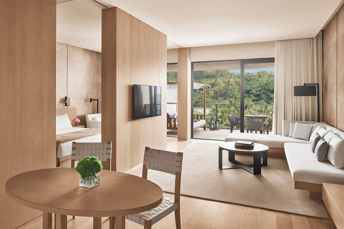 A modern hotel room with a balcony, a flat-screen TV, a sofa, and a dining area.