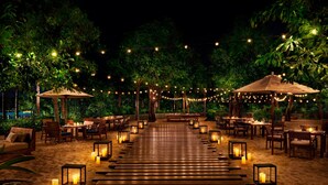 An outdoor dining area with wooden benches and tables, string lights, and lanterns. - The Sanya EDITION (Sanya)