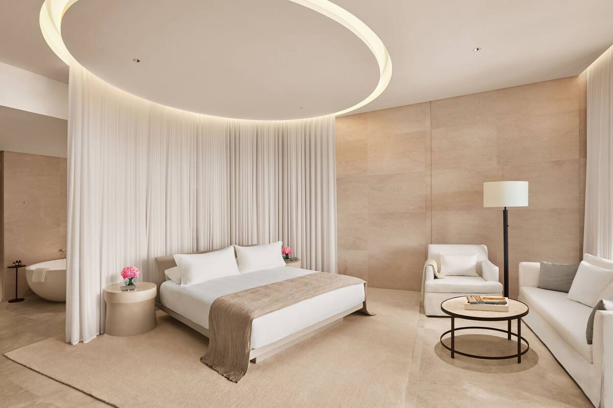 A modern hotel room with a large bed, a round coffee table, a sofa, and a floor lamp.