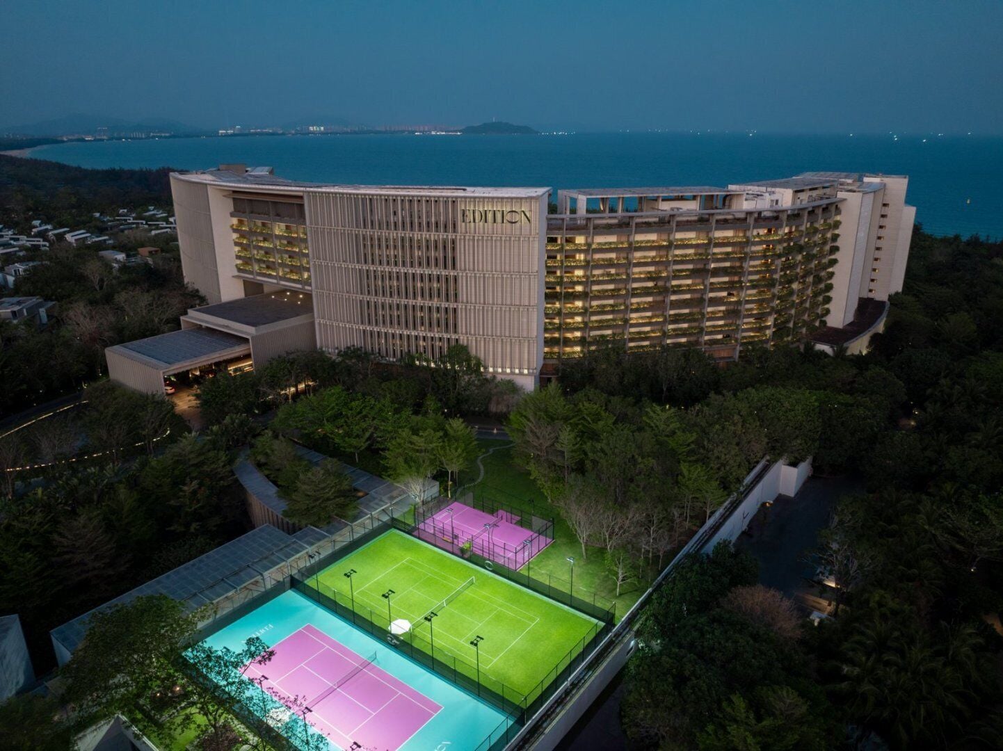 A hotel with a large building, a tennis court, and a pool.