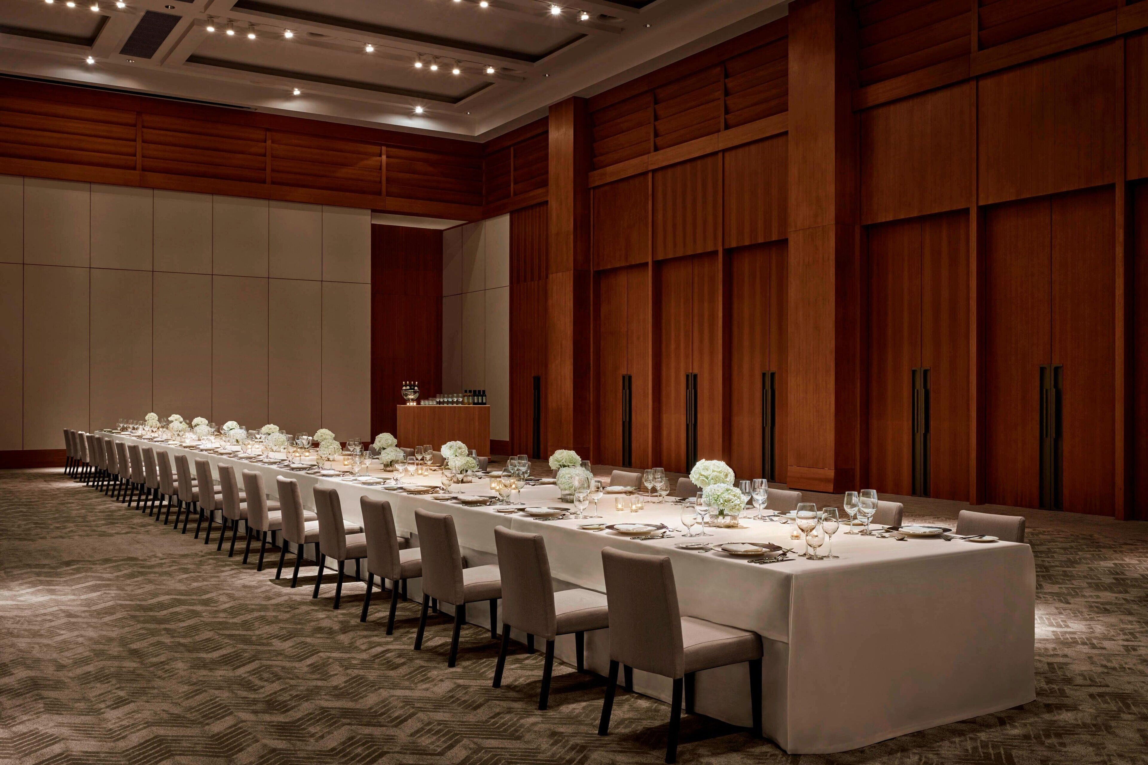 A long conference table set for a formal meeting with chairs and a podium in a room with wooden paneling and carpeted flooring.