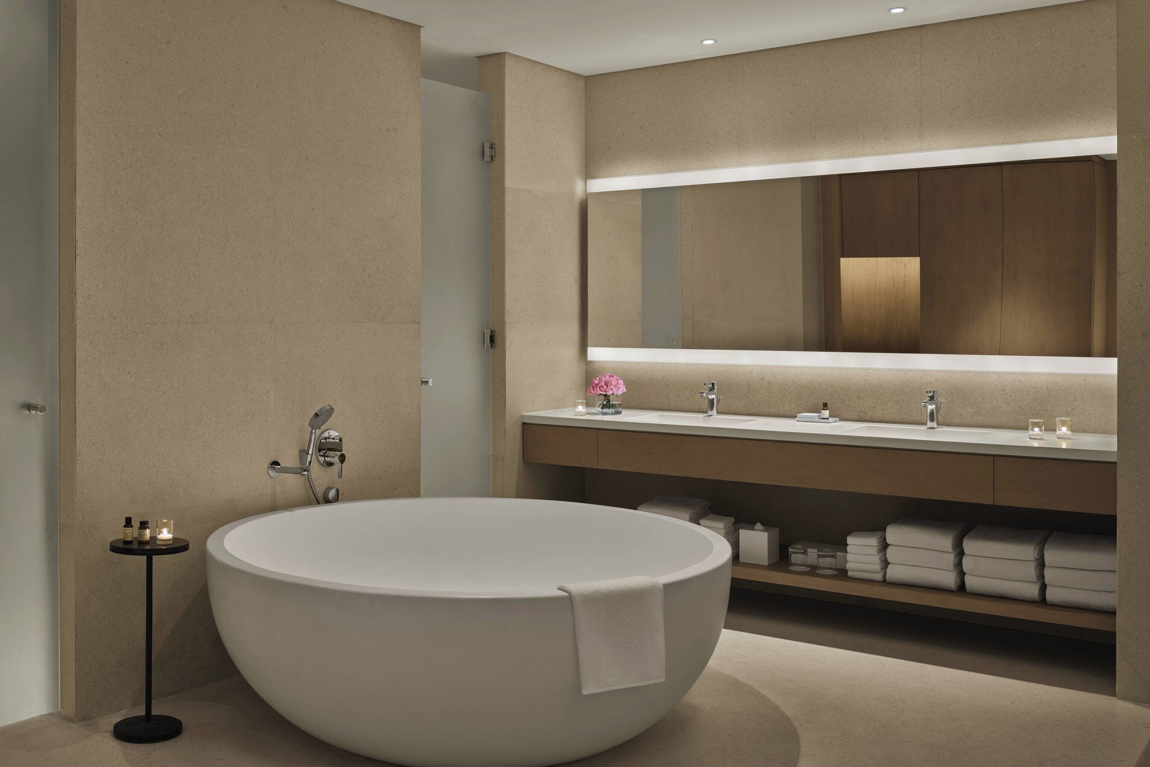 A modern bathroom with a freestanding bathtub, a large mirror, and a vanity with towels.