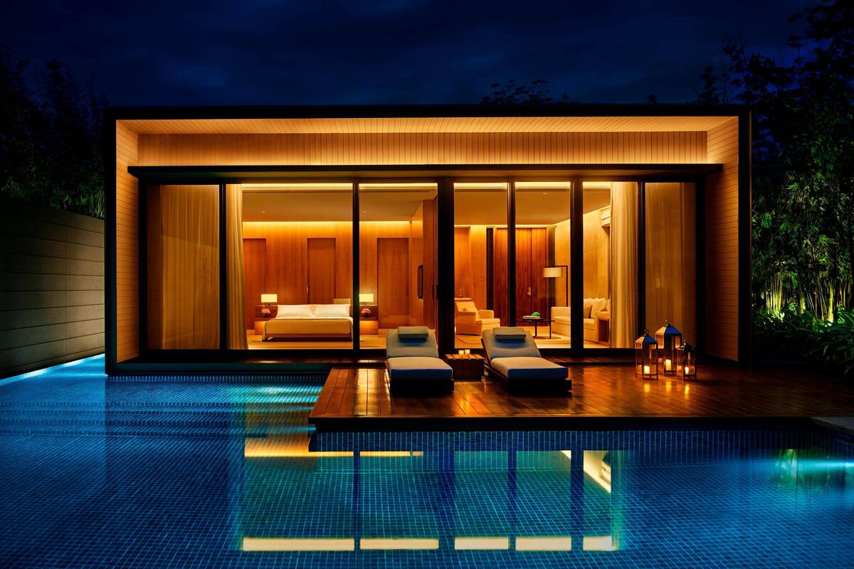 A modern house with a swimming pool, large glass windows, and a well-lit interior.