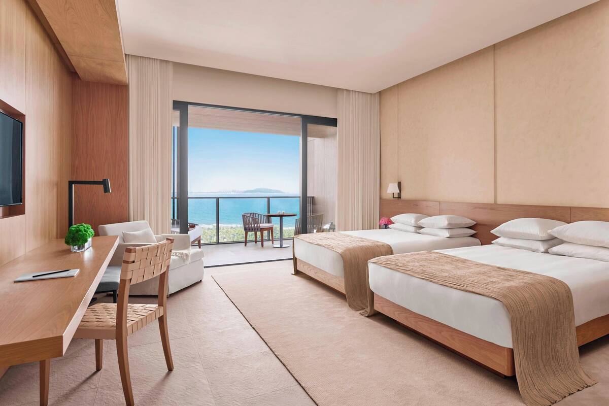 A hotel room with a large bed, a desk, a chair, and a view of the sea.