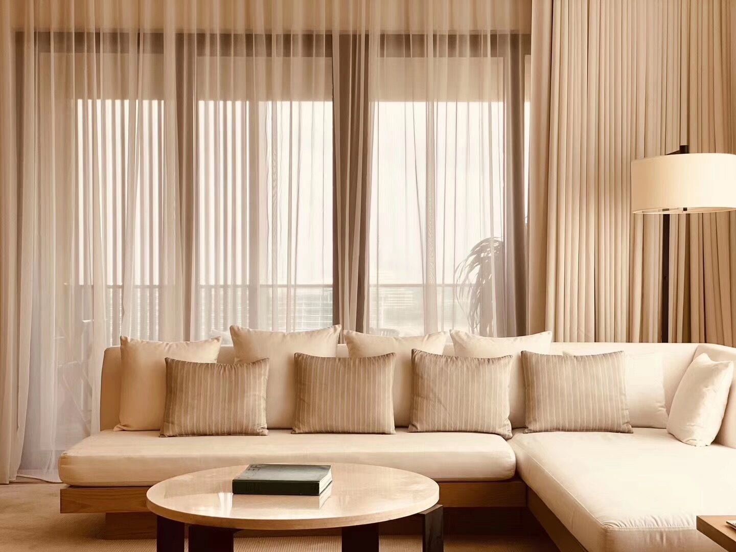 Ein modernes Wohnzimmer mit einem beigen Sofa, einem runden Couchtisch und transparenten Vorhängen.