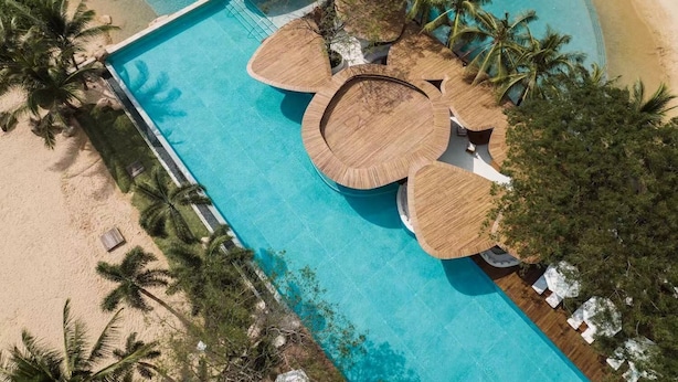 An aerial view of a resort with a central pool surrounded by palm trees and a sandy beach. - The Sanya EDITION (Sanya)