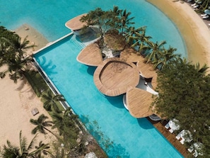 Vista aérea de un resort con una piscina central rodeada de palmeras y una playa de arena.