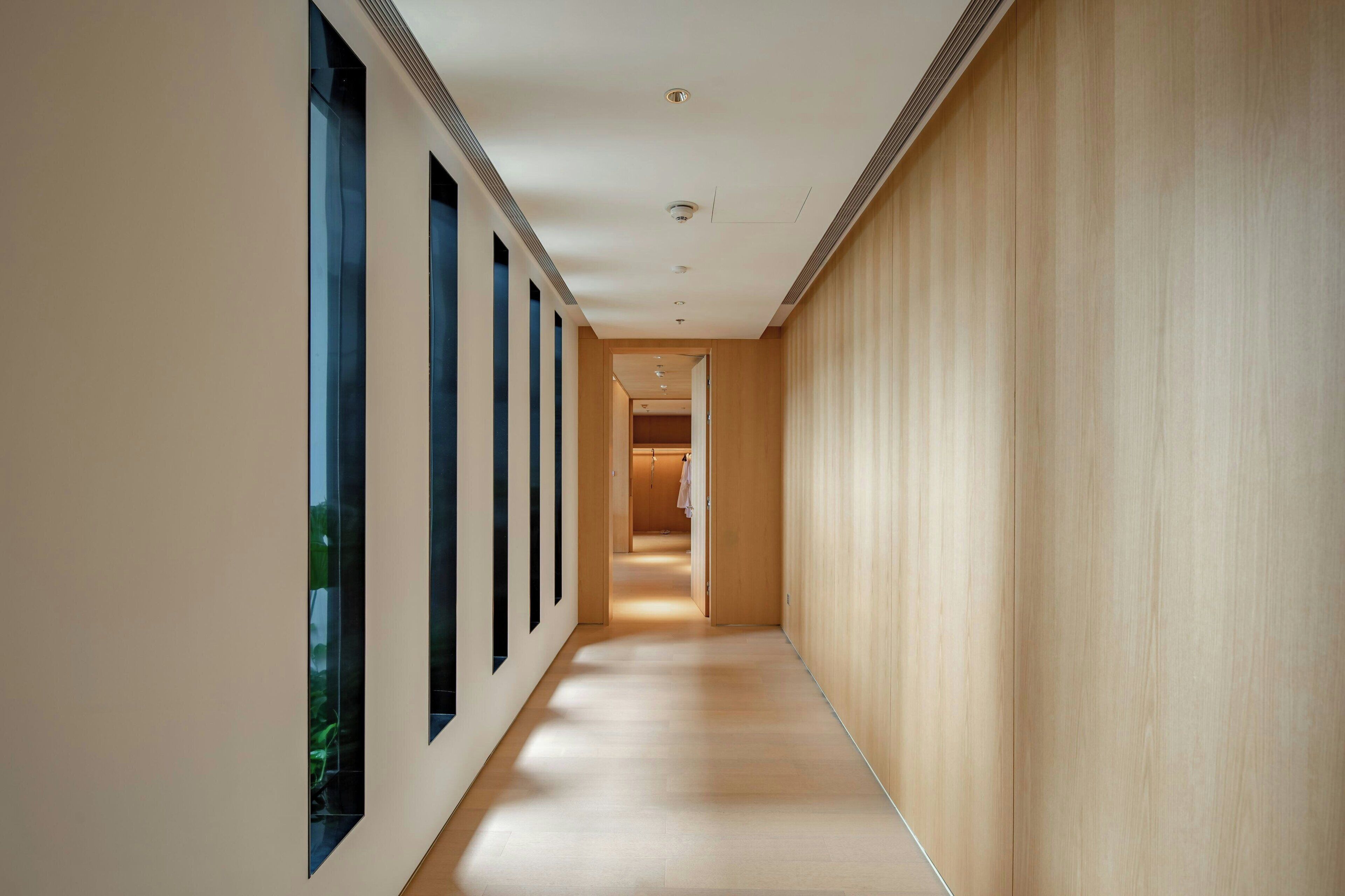 Un pasillo moderno con piso de madera, ventanas amplias a un lado y una pared de madera al otro.