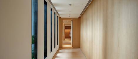 Un pasillo moderno con piso de madera, ventanas amplias a un lado y una pared de madera al otro.