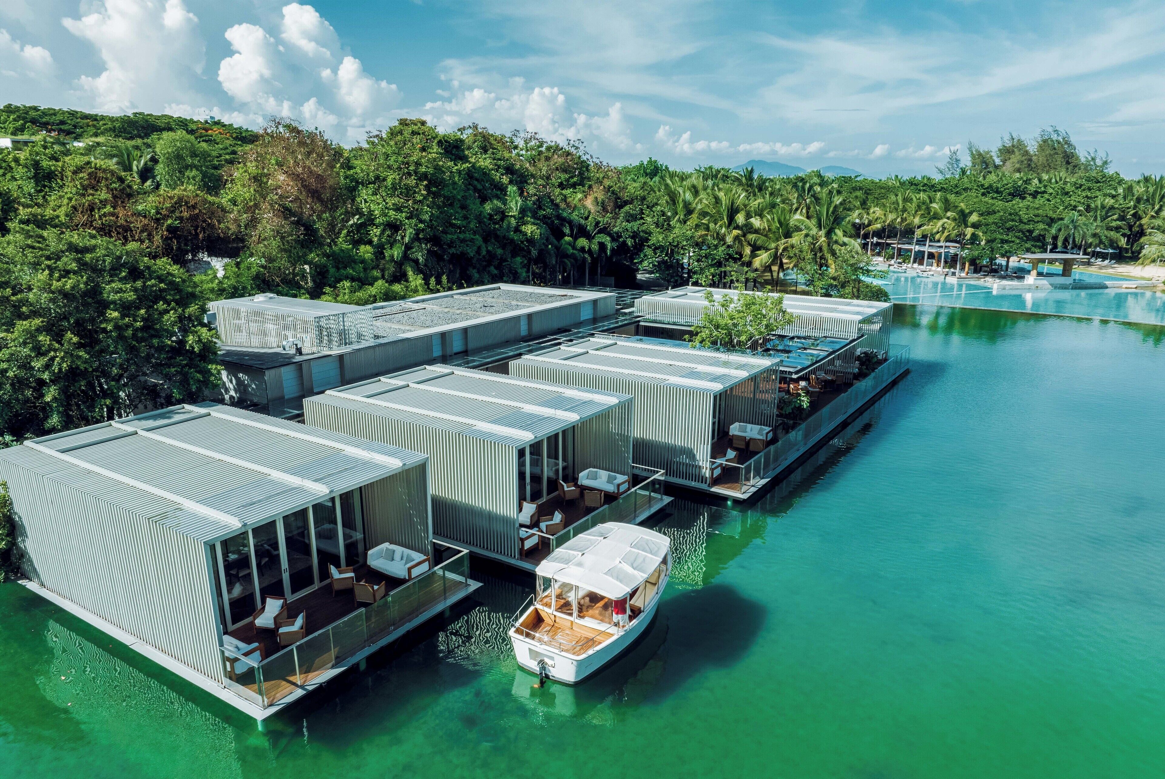 Een drijvend hotel met meerdere bungalows boven het water, verbonden door loopbruggen, elk met een zwembad en buitenzitplaatsen.