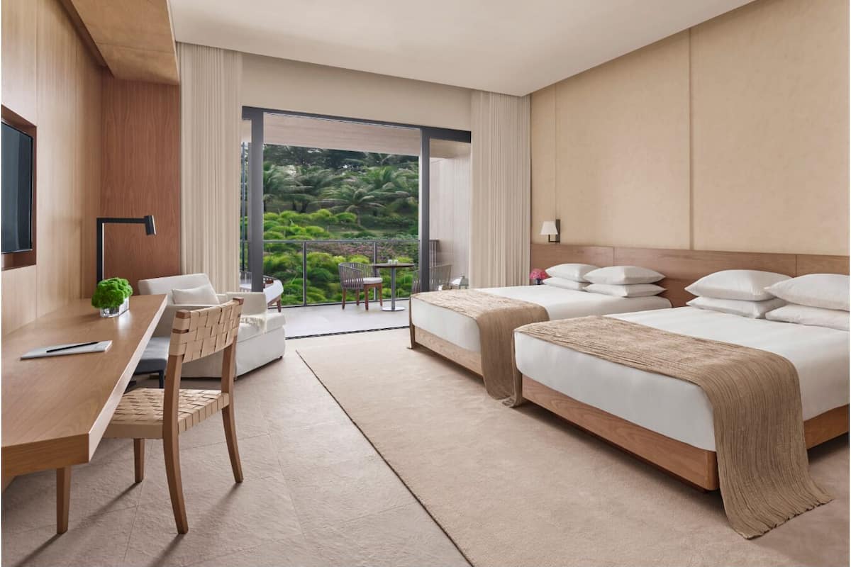 A modern hotel room with a balcony, two beds, a desk, and a chair.
