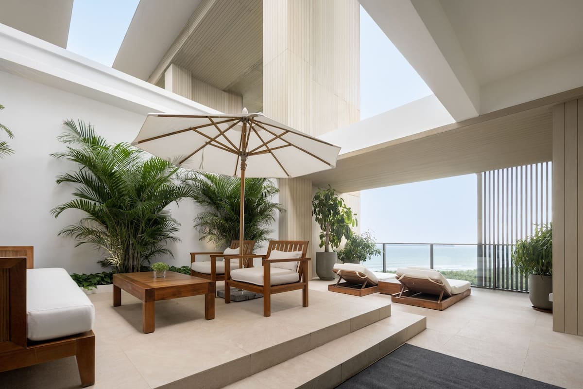 A modern outdoor lounge area with wooden furniture, a large umbrella, and potted plants.