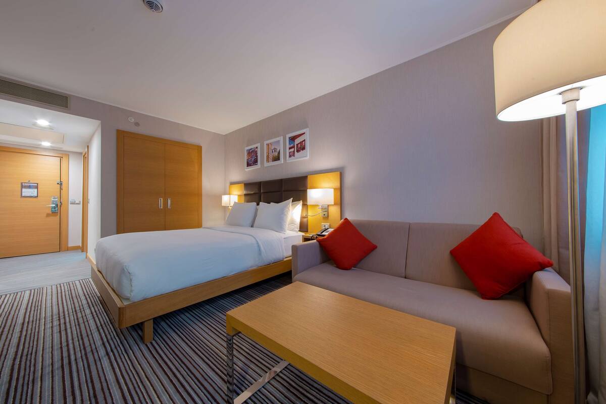 A hotel room with a bed, a sofa, a coffee table, and a lamp.