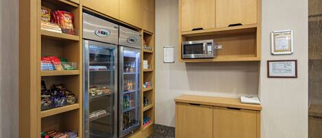 Een kitchenette met houten kastjes, een koelkast, een magnetron en een klein aanrecht.