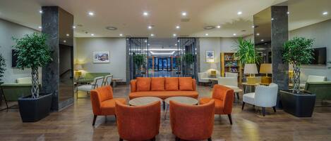 A lobby with a sofa set, chairs, and potted plants.