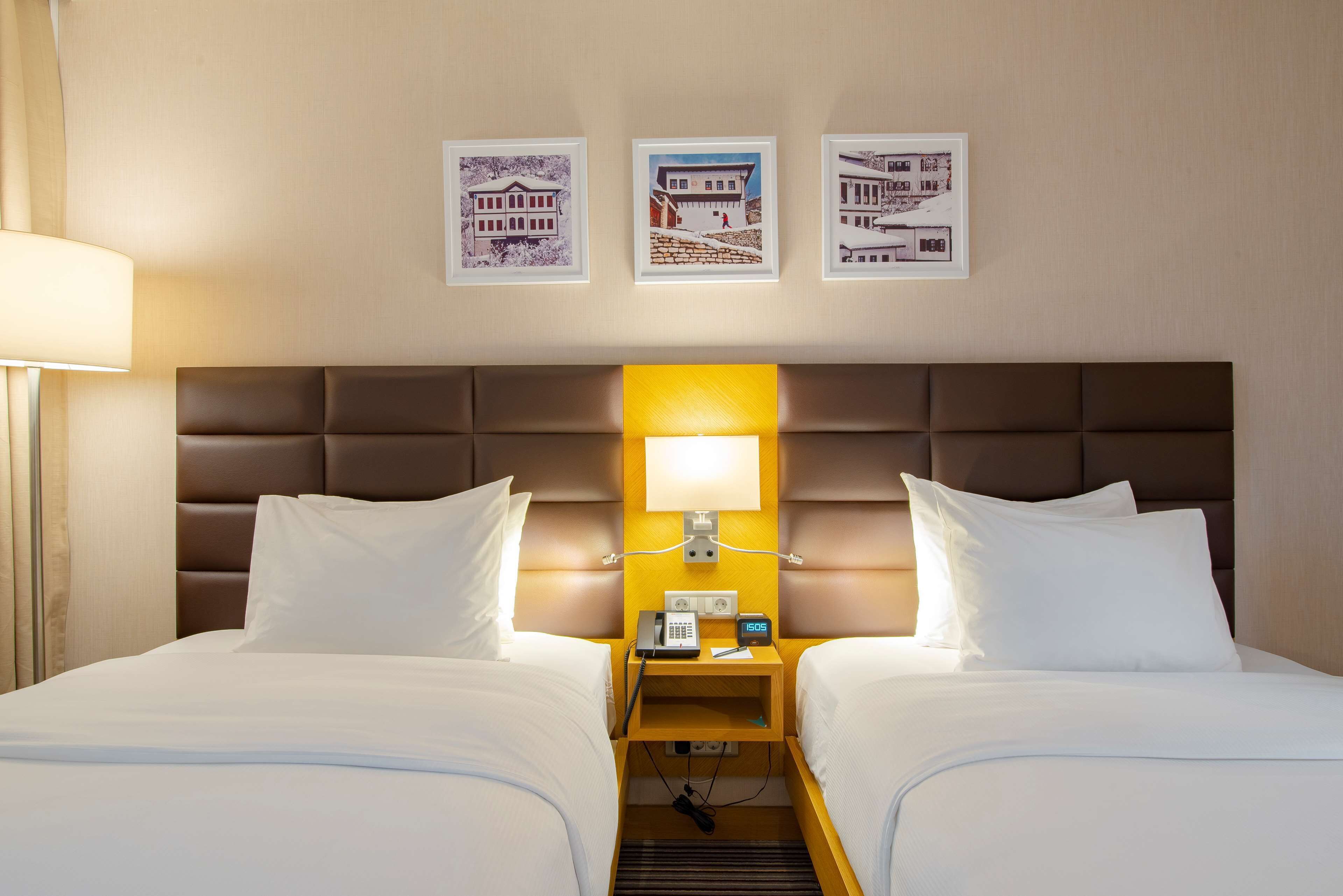 A hotel room with two beds, a nightstand with a lamp, and three framed pictures on the wall.