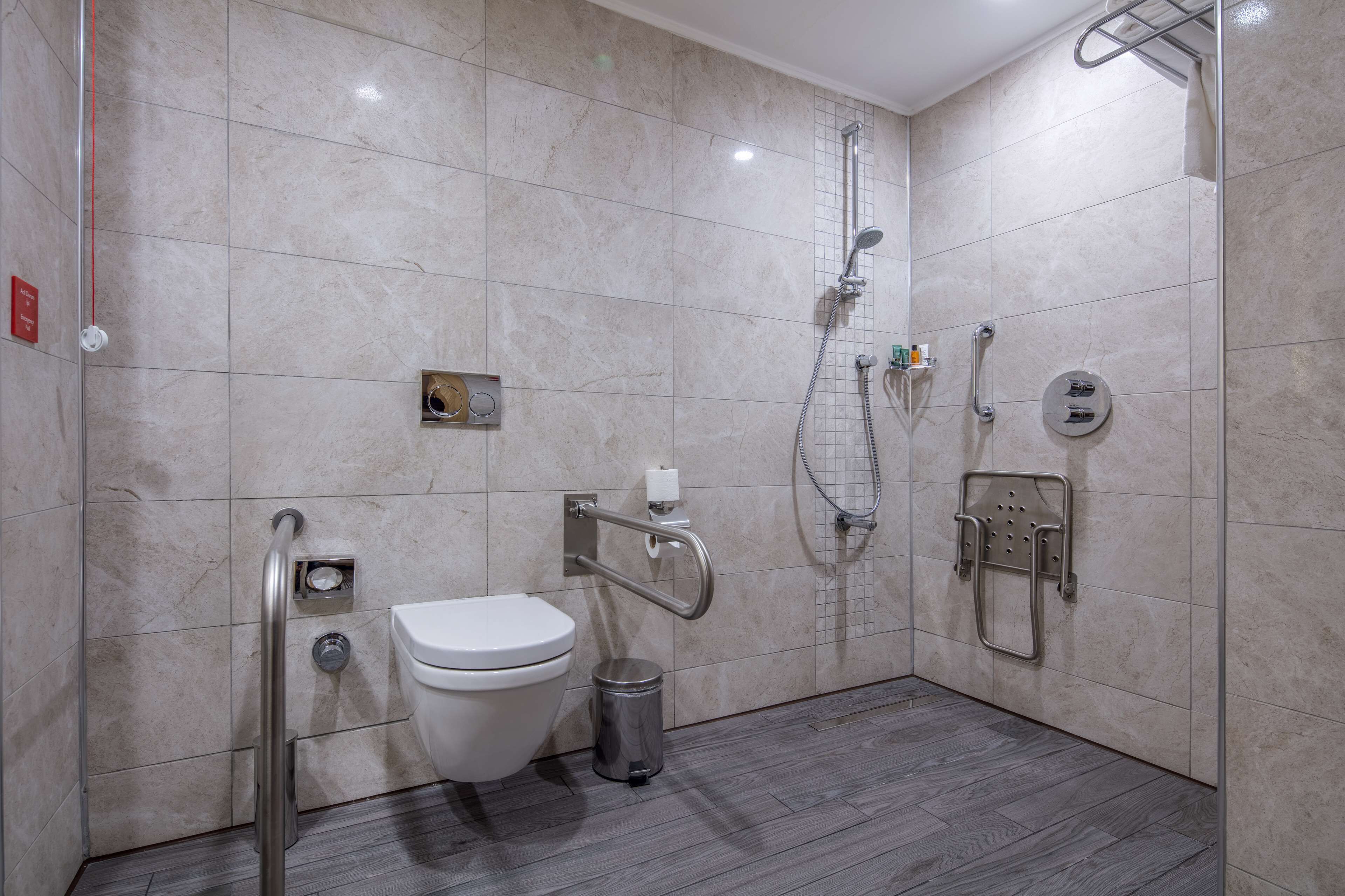 A modern bathroom with a toilet, grab bars, a shower, and a hand dryer.